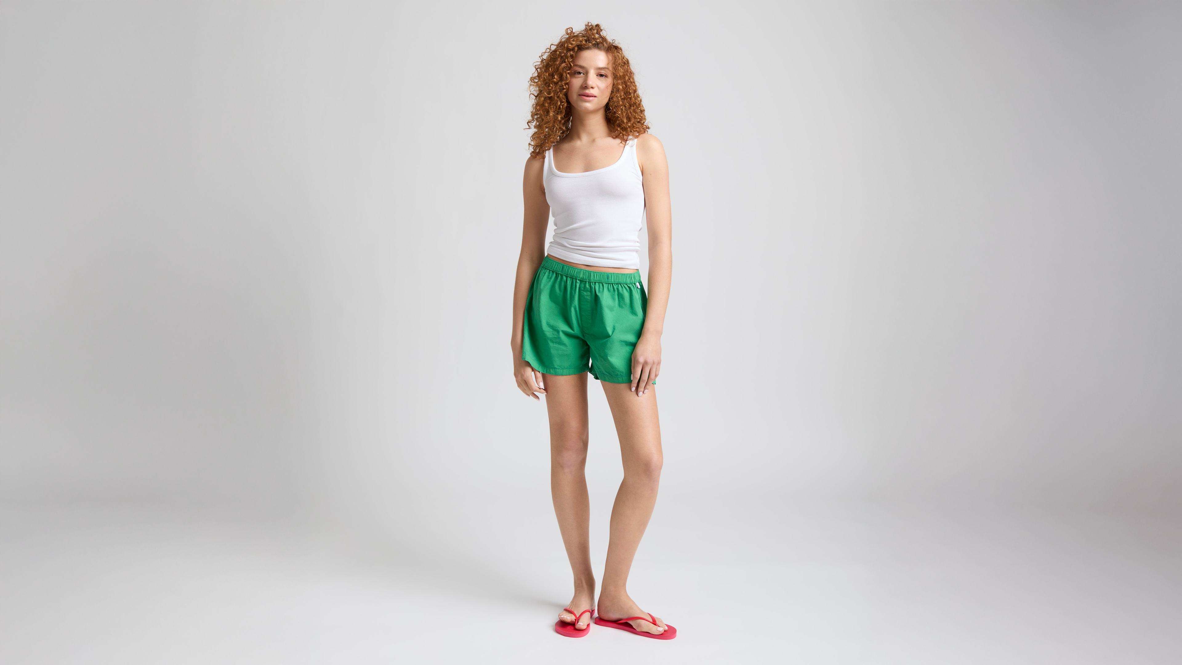 Model wearing white tank top, green Bye Boxers shorts and red flip flops